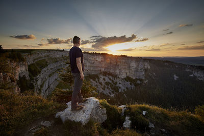 Man standing on rock against sky at sunset