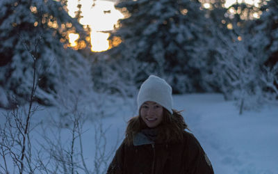 Portrait of smiling young woman standing in forest during winter