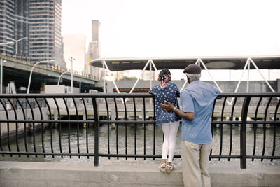 Rear view of grandfather and granddaughter standing at railing in city