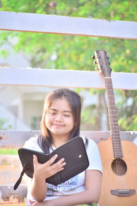 Smiling young woman using digital tablet by guitar against fence