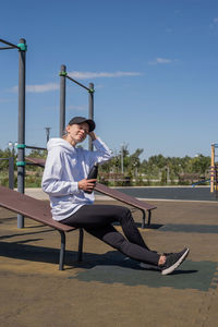 Sportive woman in sport clothes drinking water from thermos bottle on sport ground