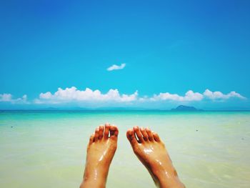 Low section of legs on beach against blue sky