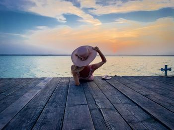 Rear view of woman with hat lying down on a wooden pontoon near the ocean at sunset