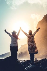 Rear view of people with arms outstretched standing against sky