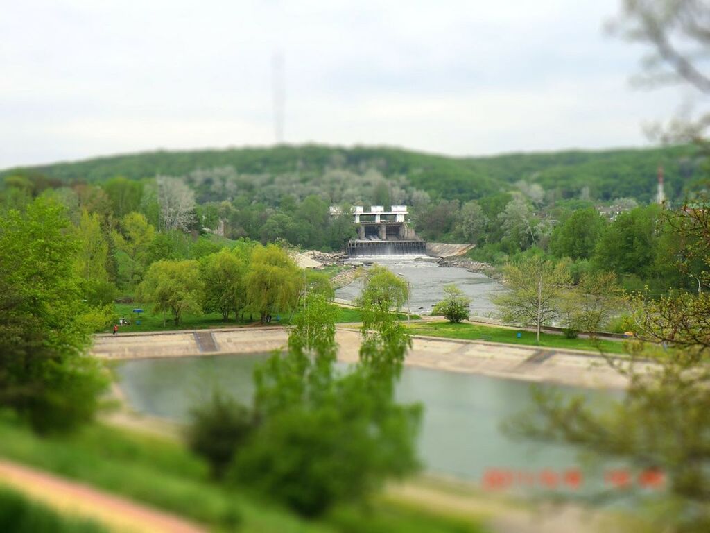 tree, architecture, built structure, water, building exterior, river, growth, green color, sky, nature, plant, waterfront, transportation, house, bridge - man made structure, day, tranquility, tranquil scene, mountain, lake