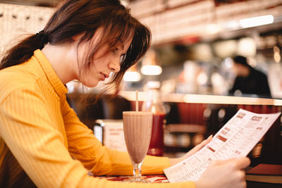 Teenage girl reading menu while sitting in restaurant