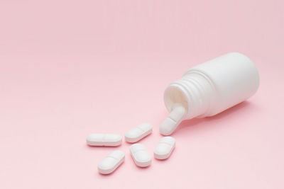 High angle view of pills spilling from bottle against pink background