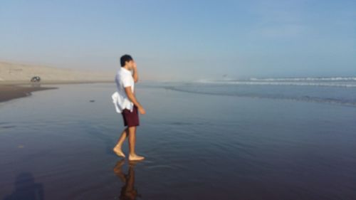 Rear view of woman standing at beach against clear sky