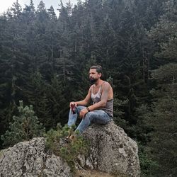 Young man sitting on rock in forest