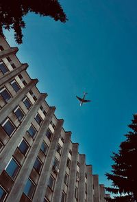 Low angle view of airplane flying over buildings against blue sky