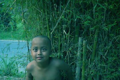 Portrait of shirtless boy sitting against plants