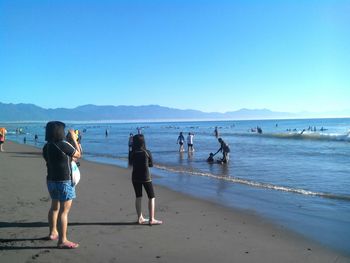 People at beach against clear blue sky