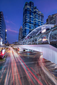 Light trails on road by buildings against sky at night