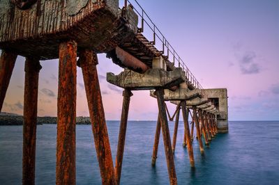 Rusty metallic columns of pier in sea against sky