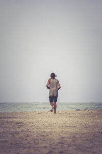 Rear view of man running on sand at beach against clear sky