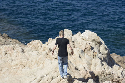 Rear view of teenage boy standing on rock formation against sea