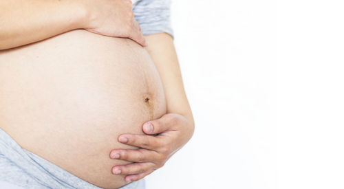 Midsection of pregnant woman touching abdomen against white background