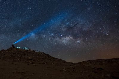 Low angle view of person standing with flashlight against sky at night