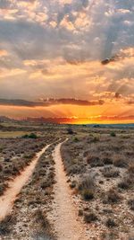Scenic view of dirt road against sky during sunset