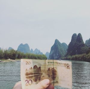 Close-up of hand holding boat in lake against mountains