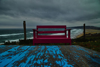 Empty bench on beach against sky