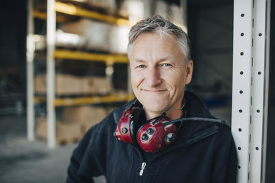 Close-up portrait of mature worker with ear protectors leaning on rack at industry