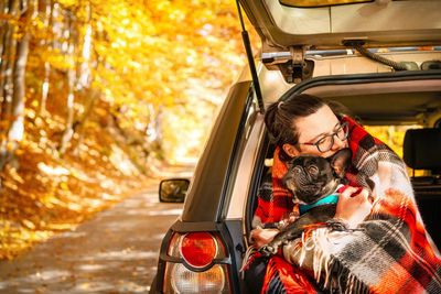 Portrait of man with french bulldog dog in car trunk on autumn forest road