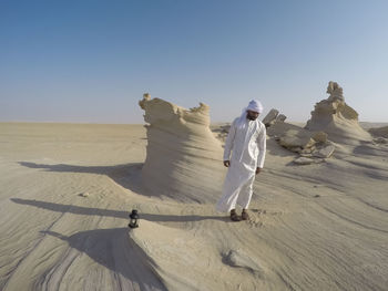 Man on sand dune in desert against clear sky