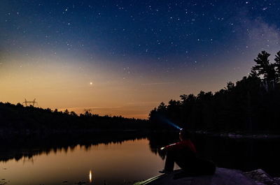 Man sitting by lake against star field in sky at night