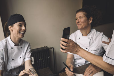 Cropped hand of chef showing smart phone to coworkers in restaurant