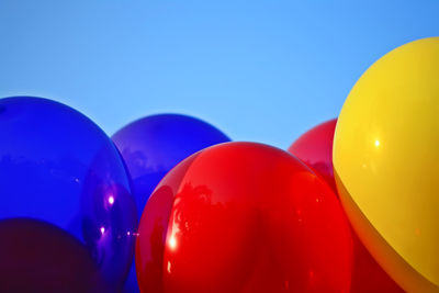 Close-up of colorful helium balloons against blue sky