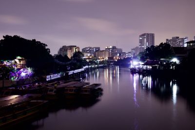 Illuminated buildings by river against sky at dusk