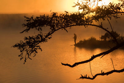 Silhouette people fishing in lake against sky during sunset