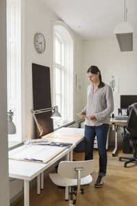 Full length of artist standing by table in creative office