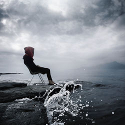 Full length of woman sitting on rock by lake against sky