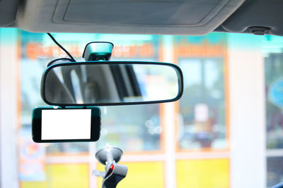 Close-up of smart phone hanging on rear-view mirror in car