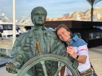 Portrait of woman leaning on sailor statue in city