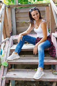 Happy woman in casual clothes is sitting on the steps on the porch and smiling.