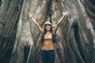 Cheerful woman standing by tree trunk