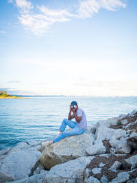 Man sitting on rock by sea against sky