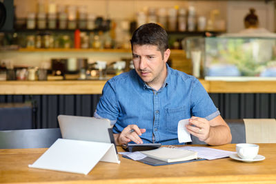Man using calculator while looking at digital tablet