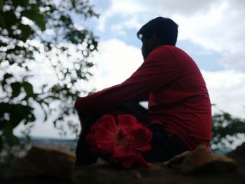 Rear view of man with red flower against sky