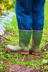 Low section of person wearing rubber boots standing on grassy field