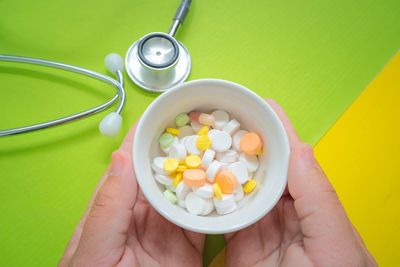 Close-up of person hands holding medicine in container by stethoscope over colored background