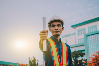 Portrait of young man holding camera against sky