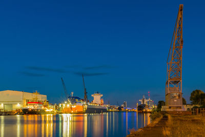 Illuminated city against clear blue sky at night