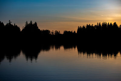 Silhouette trees by lake against sky during sunset