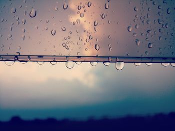 Close-up of raindrops on window against sky during rainy season