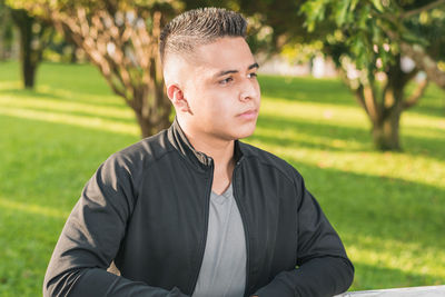 Young man looking away while sitting on park