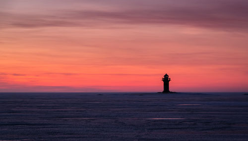 Lighthouse by sea against romantic sky at sunset